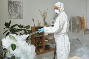 A person in protective gear disinfects a room with a fumigation tool, ensuring safety and hygiene.